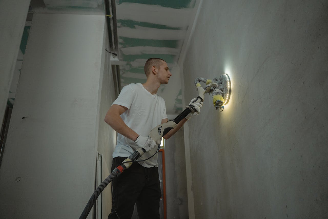 A man sanding an interior wall with an automatic sanding tool during renovation work indoors.