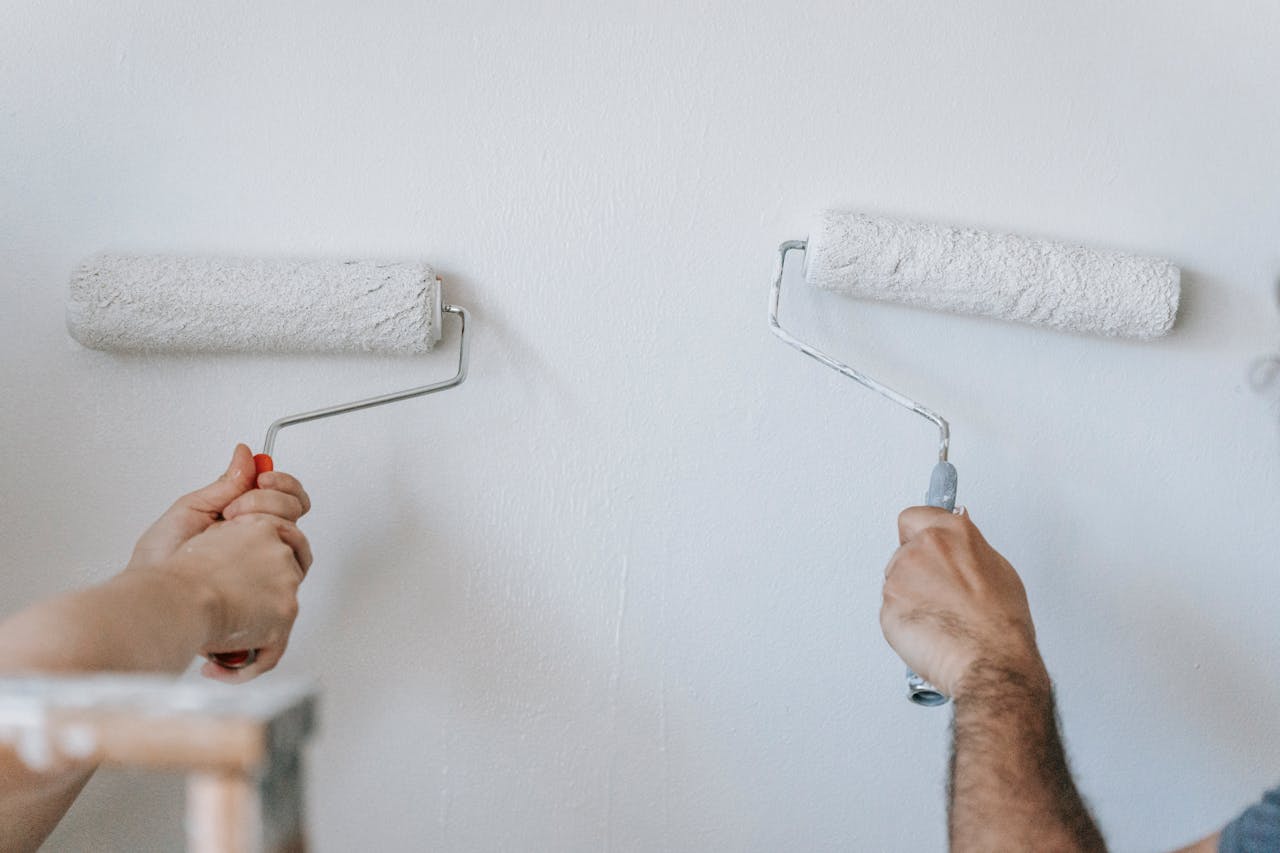 About Close-up of two individuals painting a wall with paint rollers indoors.